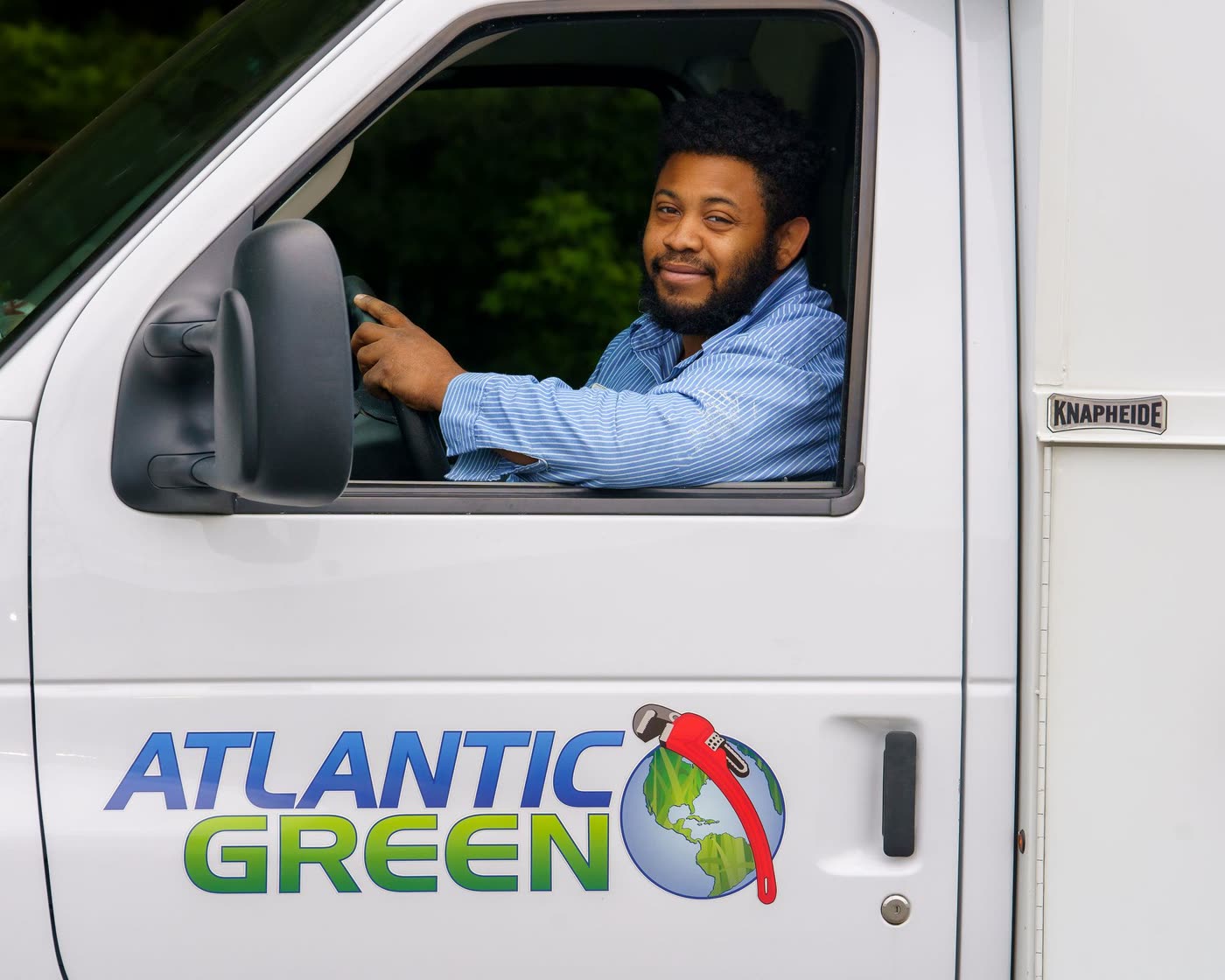 A smiling Atlantic Green technician at the wheel of a service truck