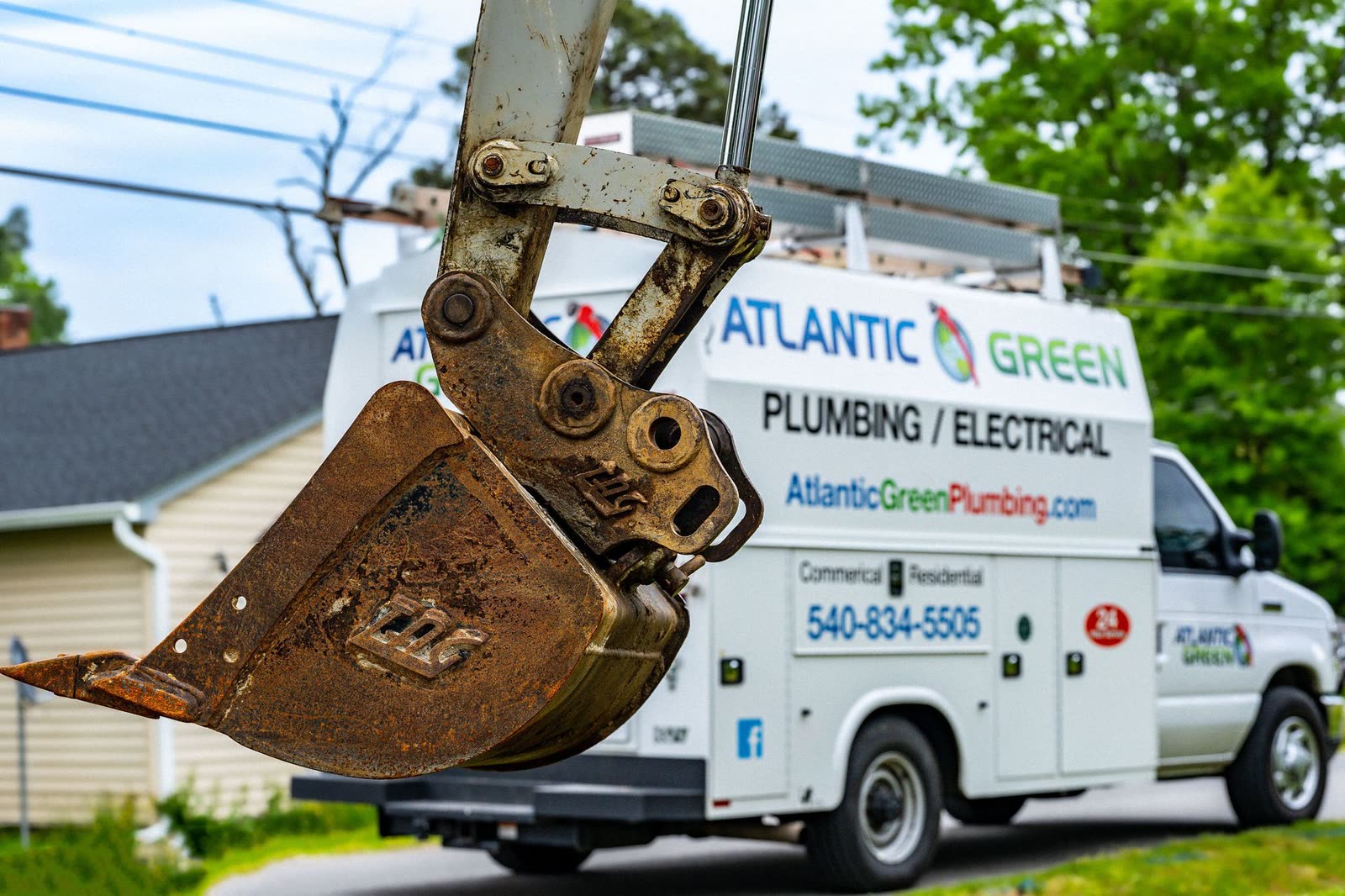 An excavator bucket raised beside an Atlantic Green Plumbing / Electrical service truck