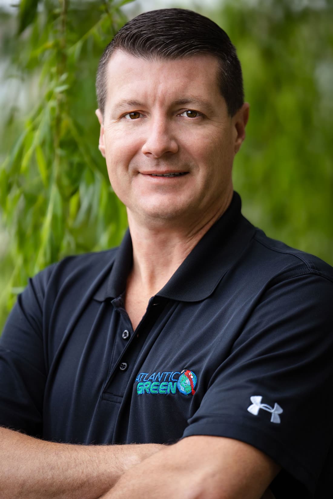 Portrait of a smiling man in a black Atlantic Green polo shirt outdoors