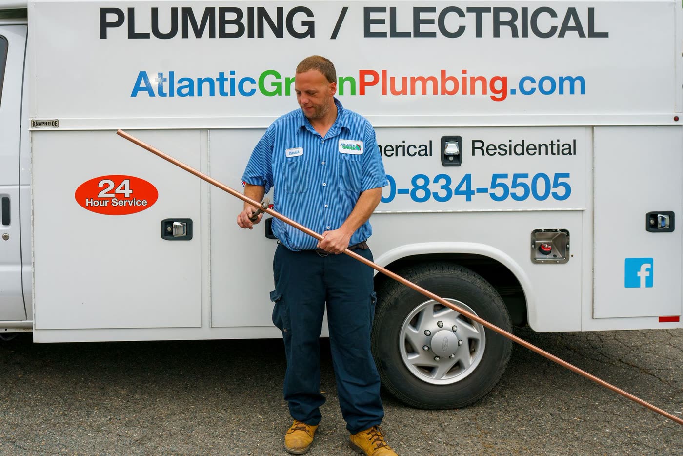An Atlantic Green plumber holding a length of copper pipe beside the service truck