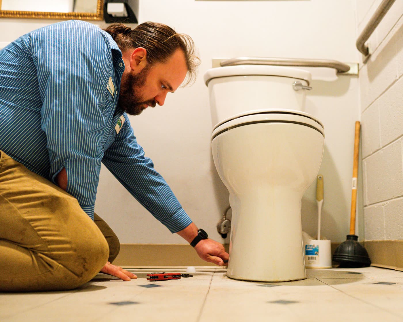 An Atlantic Green plumber kneeling beside a toilet, working on the floor connection